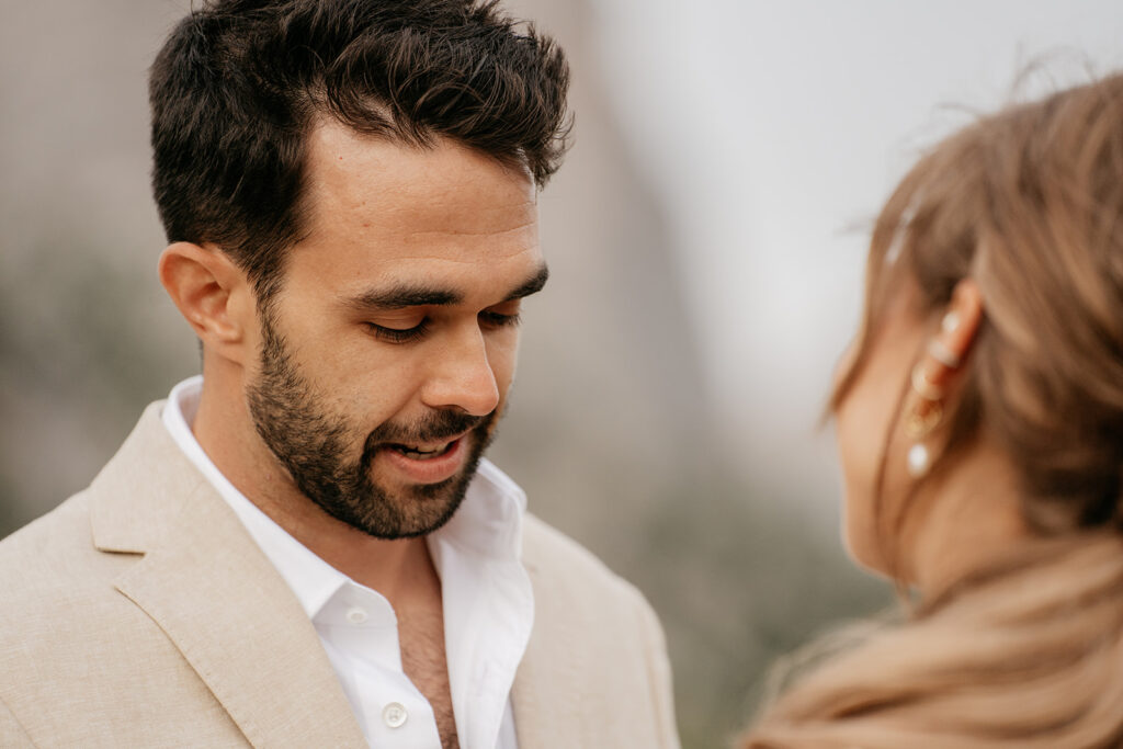 Man in beige suit speaking to woman outdoors.