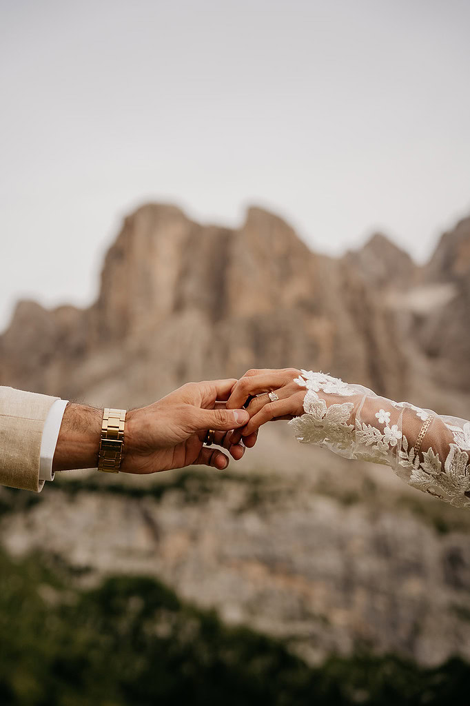 Couple holds hands before scenic mountain backdrop.