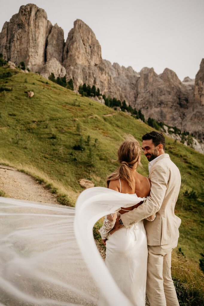 Bride and groom embrace in front of rocky mountains.