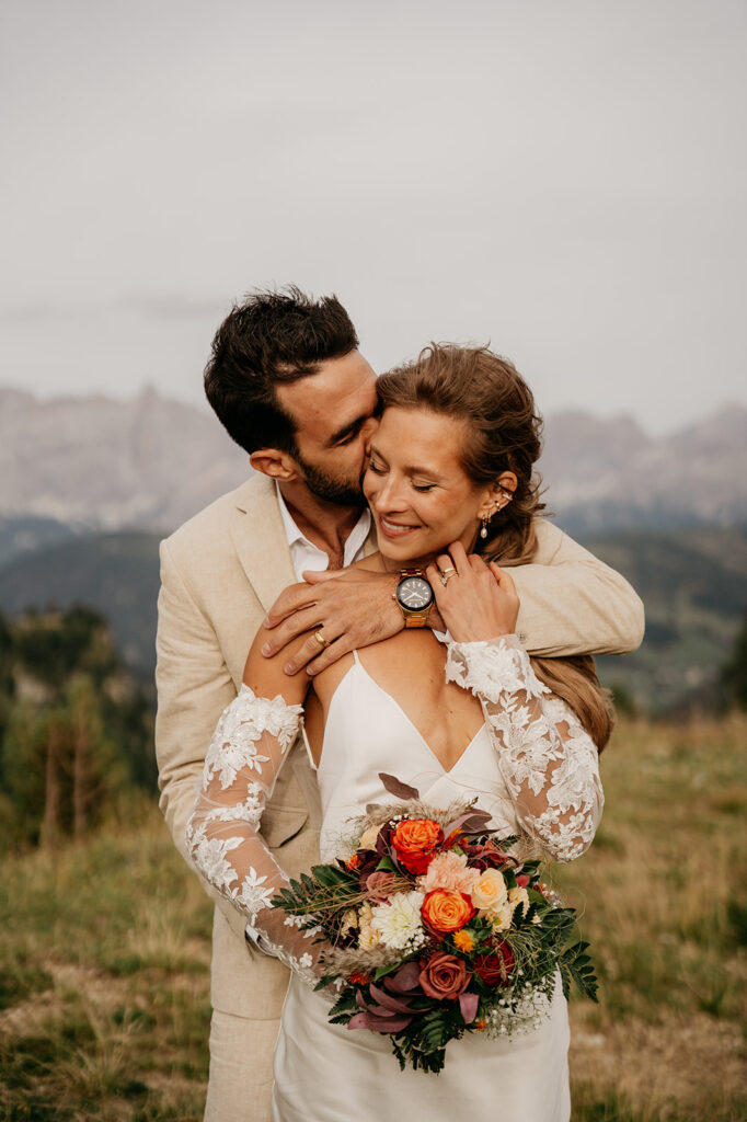 Bride and groom embracing with bouquet outdoors.