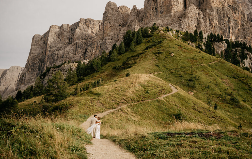 Couple embraces on mountain path with scenic cliffs.