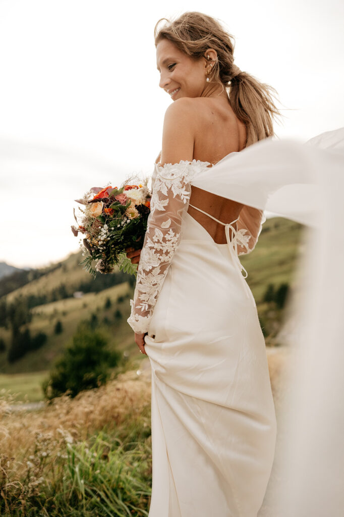 Bride in lace wedding dress holding bouquet outdoors.