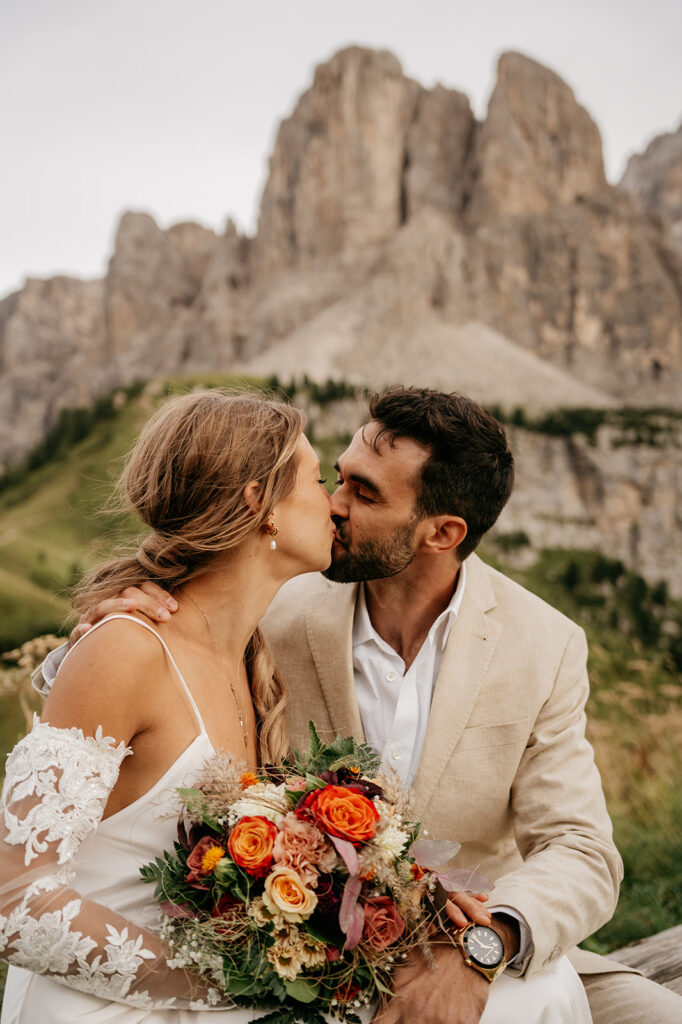 Couple kissing outdoors with flowers and mountain view.