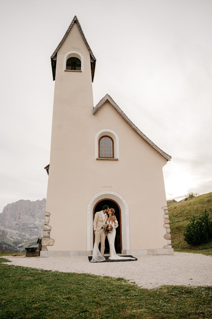 Couple kissing in front of small church entrance.