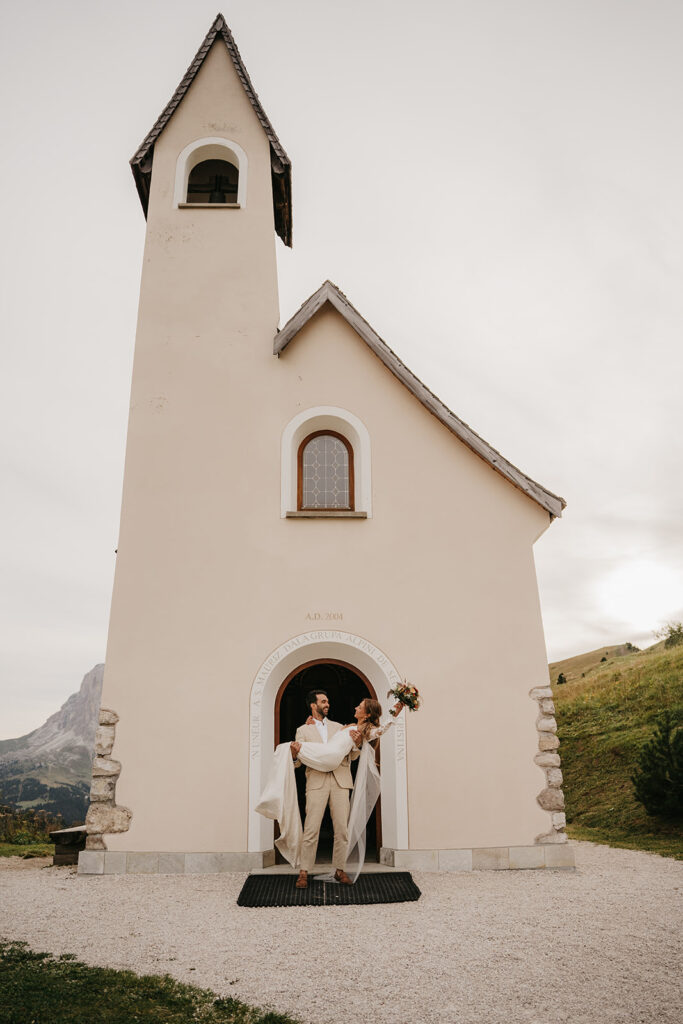 Happy couple outside small white chapel.