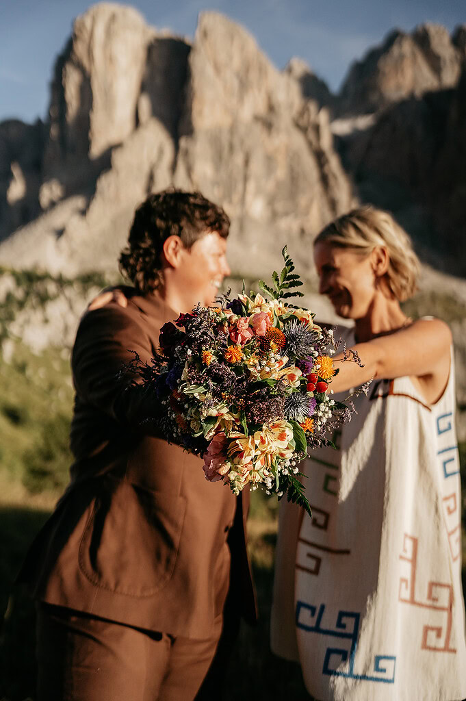 Couple holding colorful bouquet, mountain background.