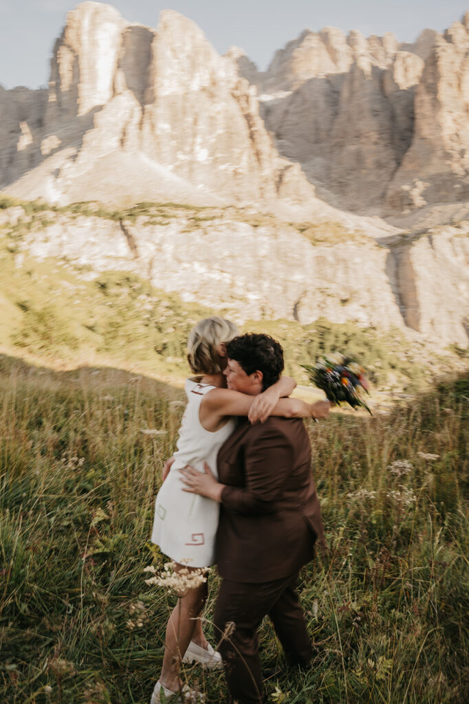 Couple embraces in mountain meadow with bouquet