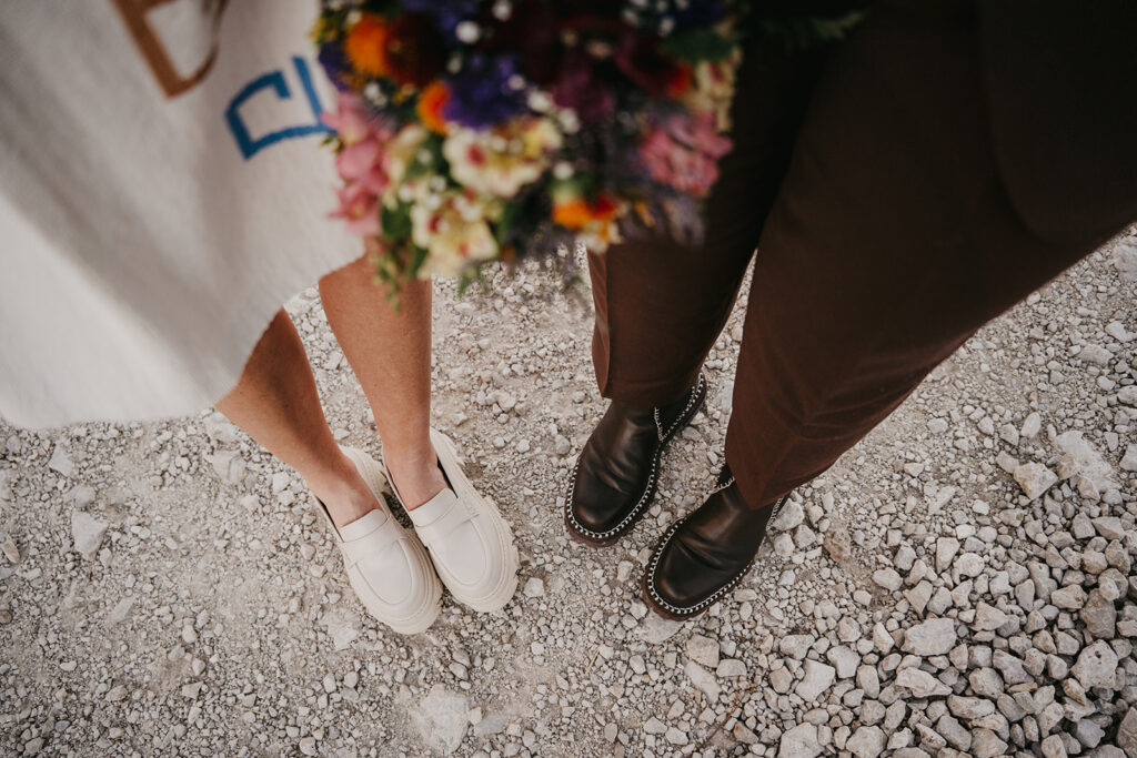 Couple's shoes on gravel with colorful bouquet.