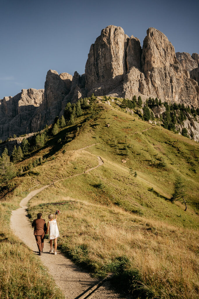 Couple walking on mountain trail under blue sky.