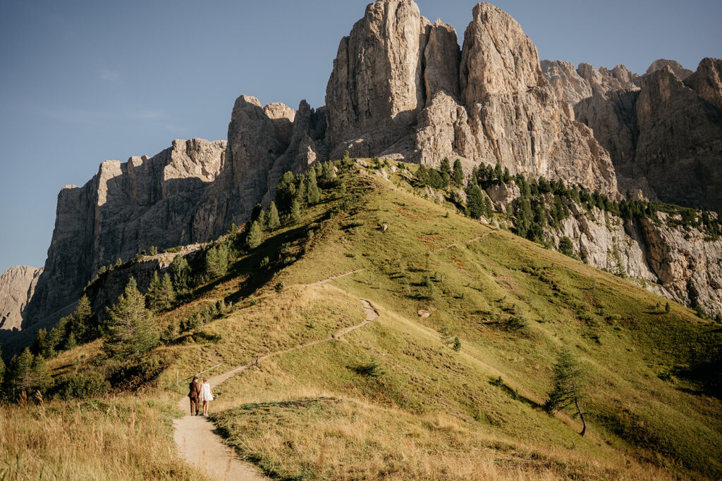 Couple walking on mountain trail with rocky peaks.