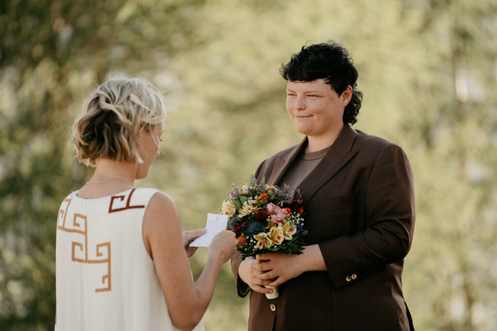 Couple exchanging vows with bouquet outdoors.