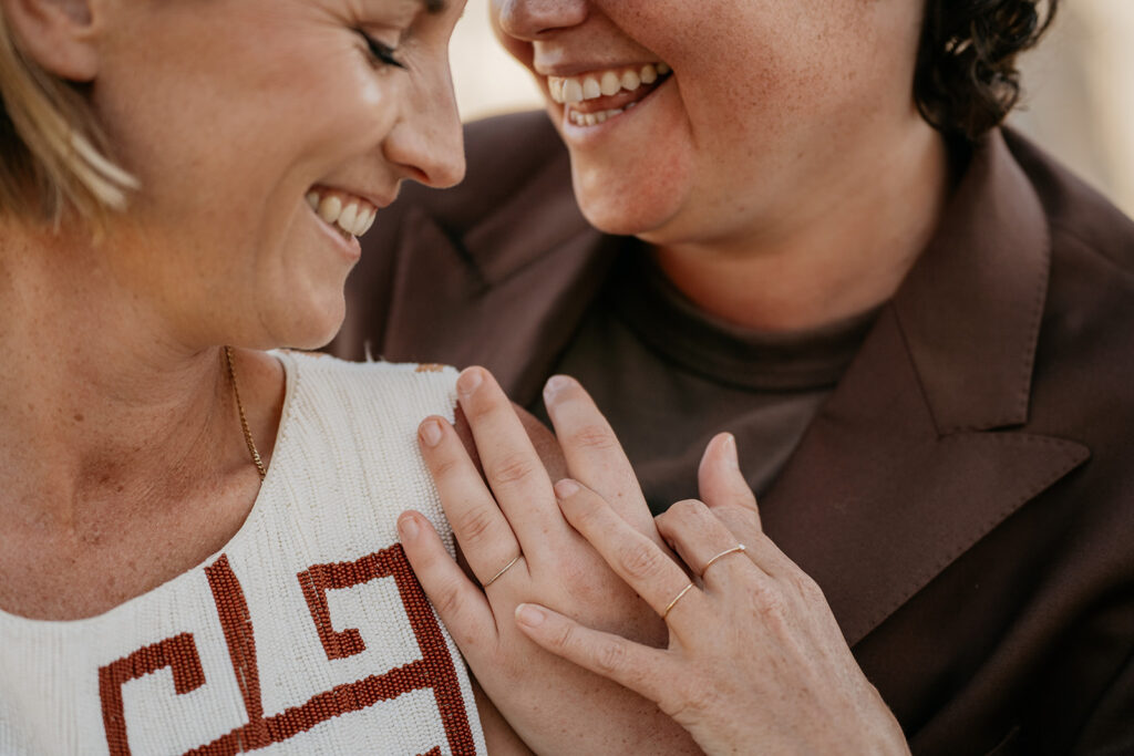 Two people smiling, wearing rings, in close embrace.