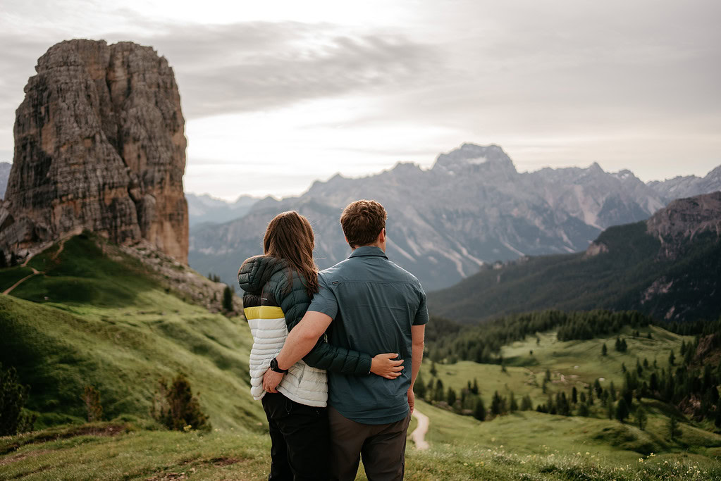 Couple embraces, overlooks mountains and green landscape.