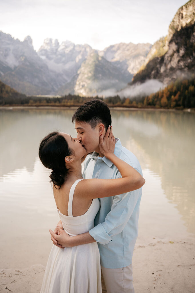 Couple kissing by a serene mountain lake.