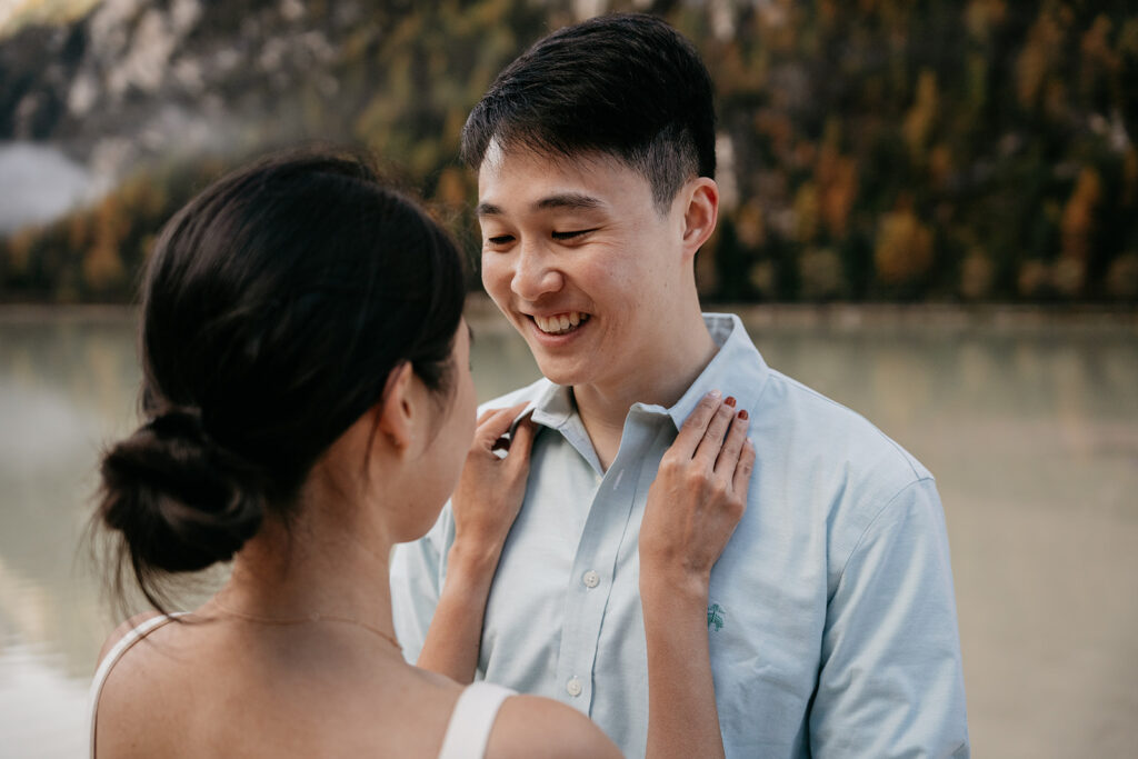 Couple smiling by a lake with autumn trees.