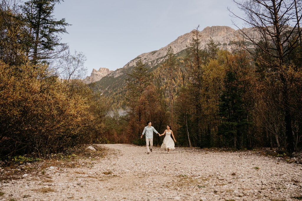 Couple walking hand in hand through forest path.