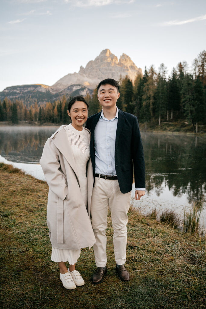 Couple smiling by mountain lake at sunrise.