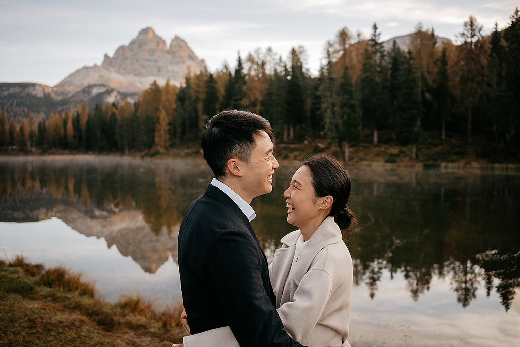 Couple smiling by lake with mountain backdrop.