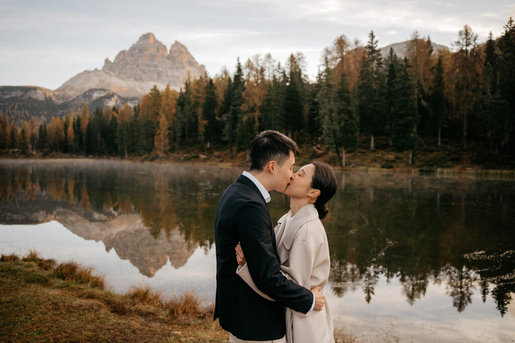 Couple kissing by forested lake and mountain view.