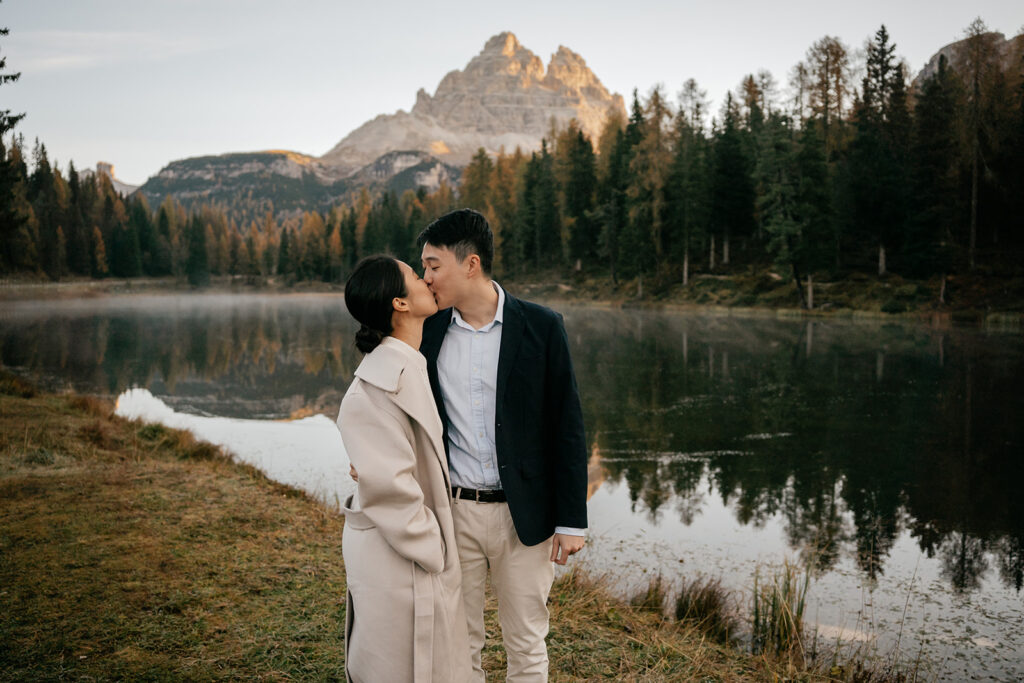 Couple kissing by mountain lake at sunrise.