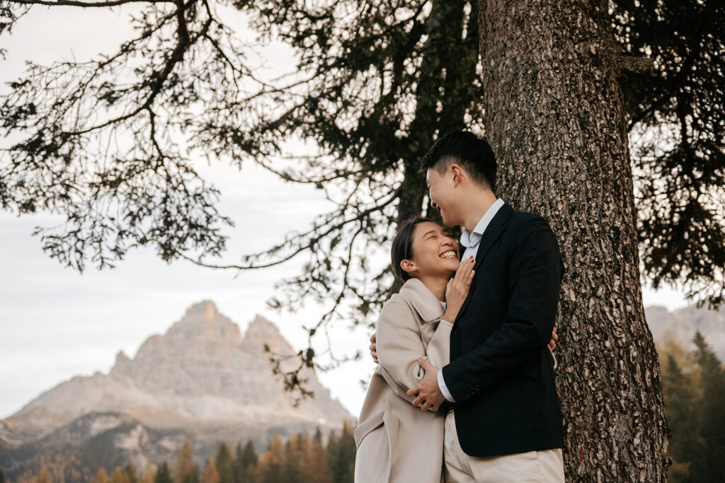 Couple smiling under a tree in the mountains.