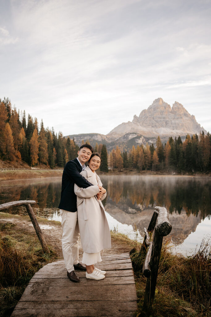 Couple embracing on bridge by lake and mountains.