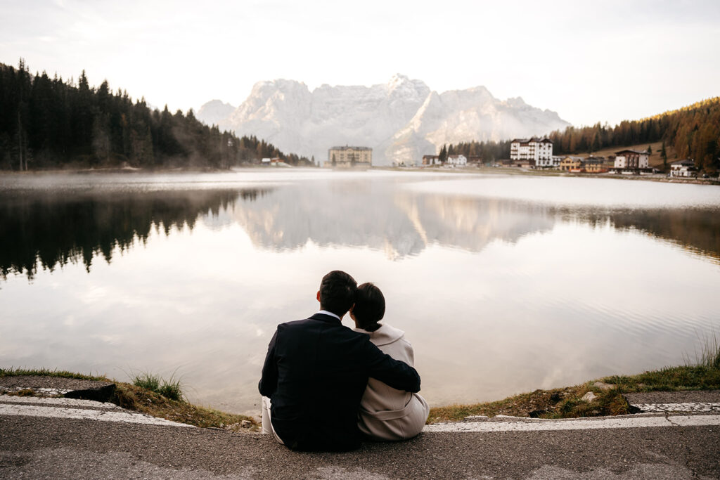 Couple sitting by serene mountain lake at sunset.