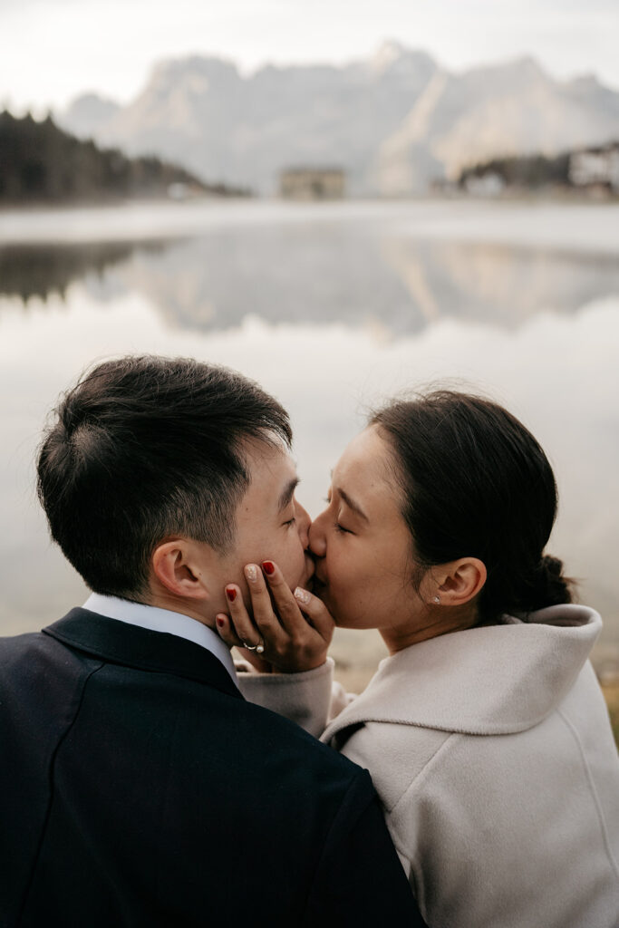 Couple kissing by a serene lake backdrop.