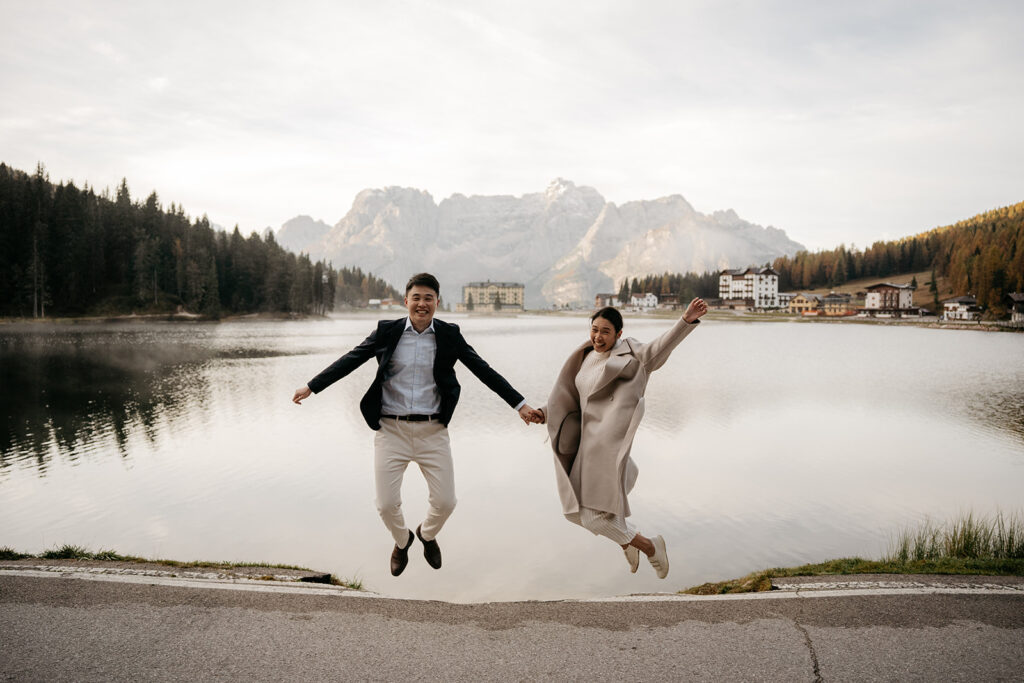 Couple jumps joyfully by scenic mountain lake.