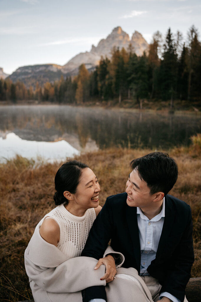 Couple laughing by mountain lake at sunset.