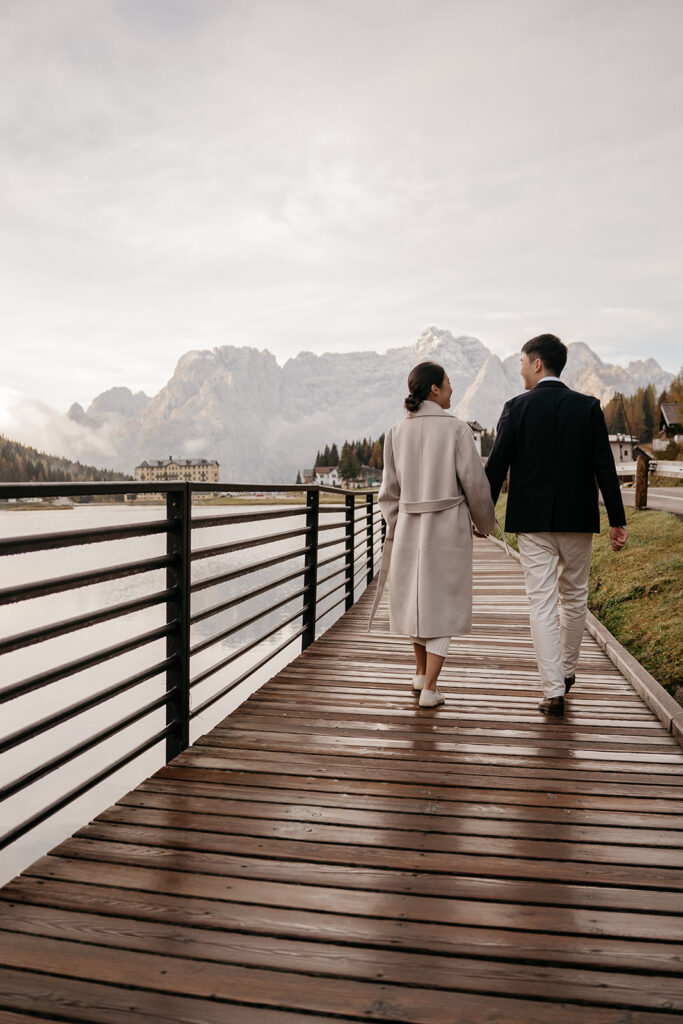 Couple walking by lake with mountain backdrop.