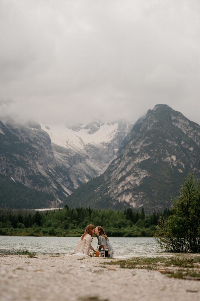 Couple kissing by mountain lake under cloudy sky.