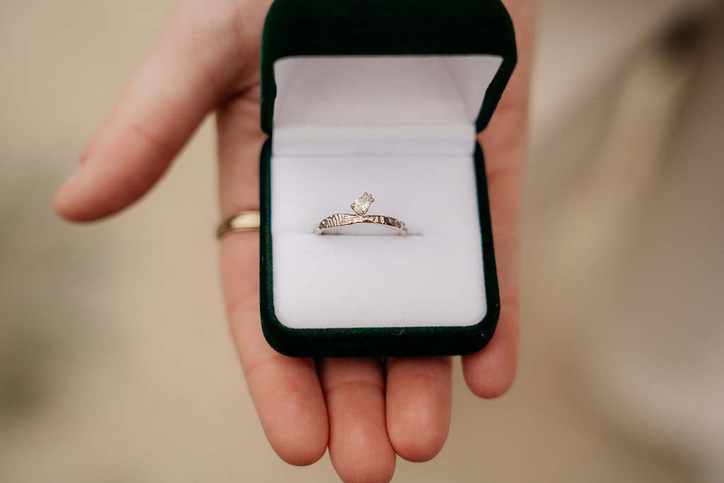 Hand holding engagement ring in green box