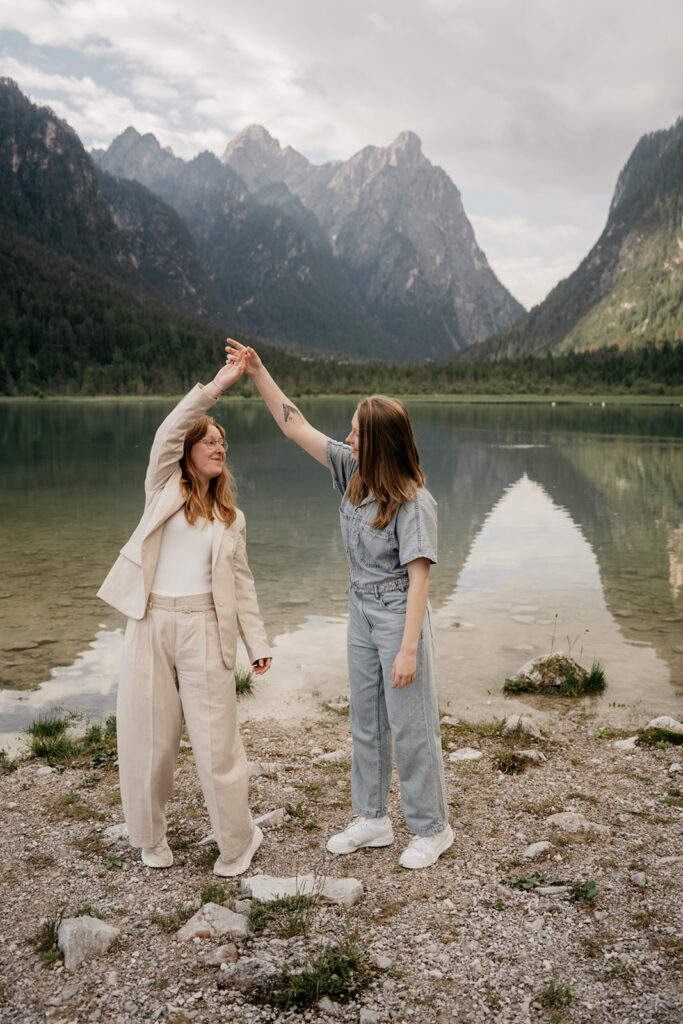 Two women dancing by a lake with mountains.