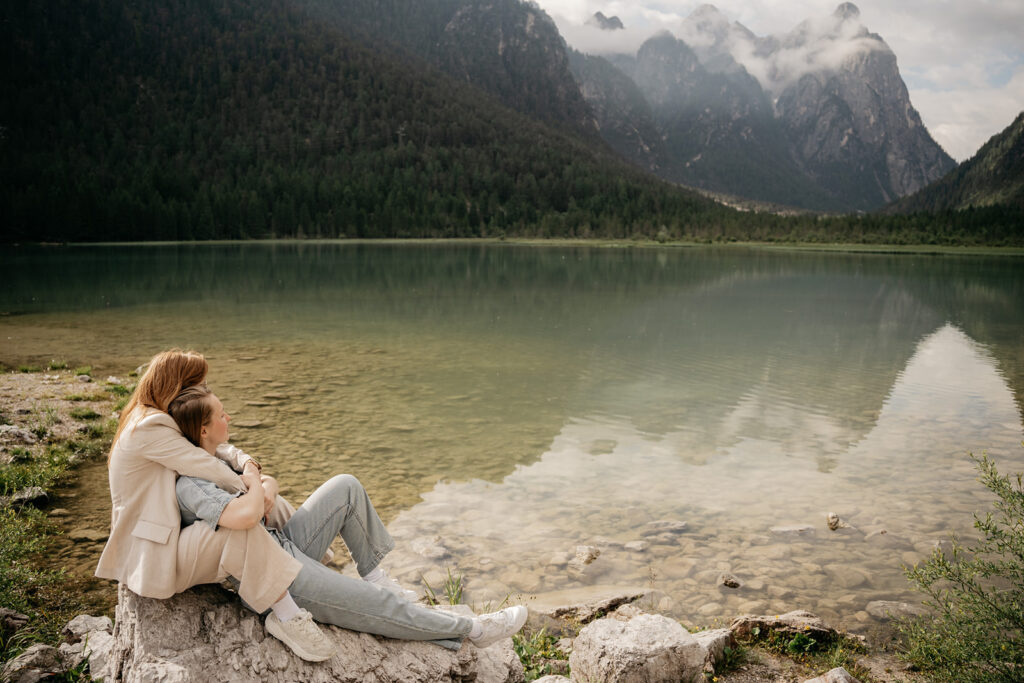 Couple embracing on rocky lakeside with mountain view.