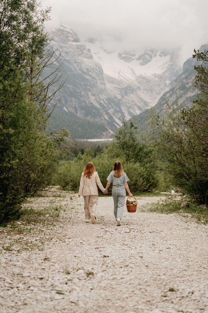 Two women walking in a mountain trail, holding hands.