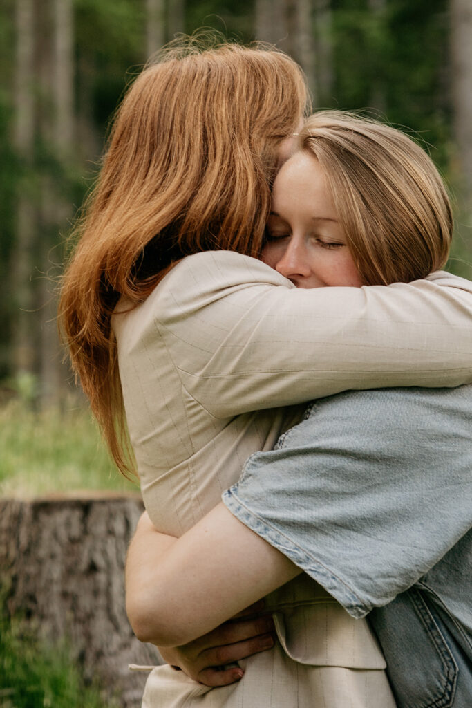 Two people hugging outdoors with closed eyes.