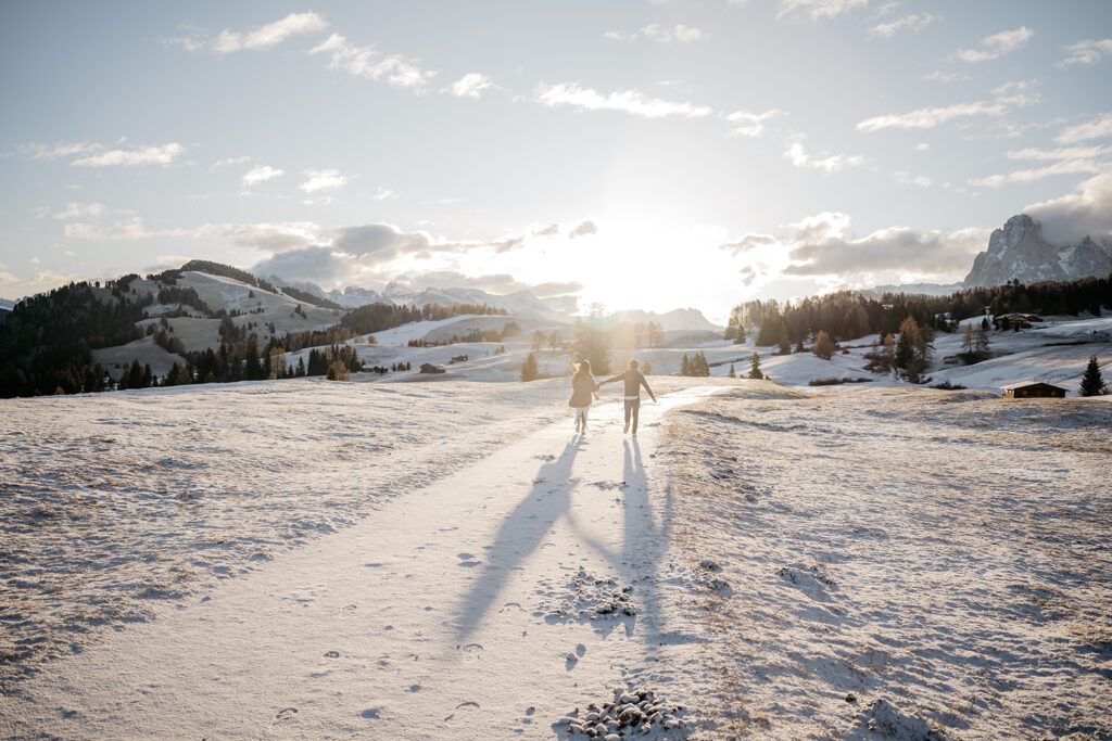 Couple walking on snowy path, mountains in background.