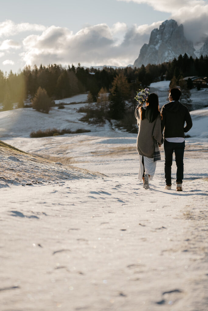 Couple walks on snowy mountain path.