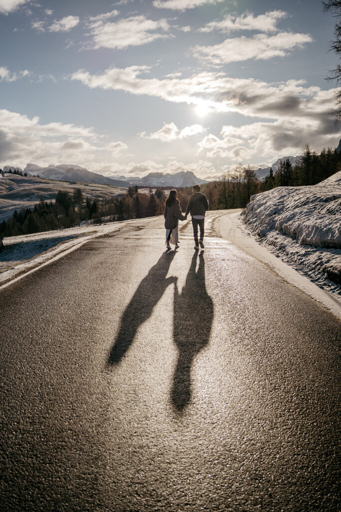 Couple walking on snowy mountain road at sunset.