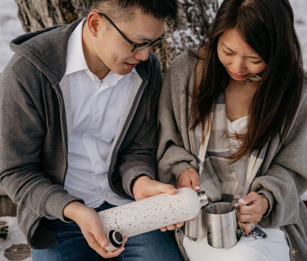 Couple pouring drink from flask into mug outdoors.