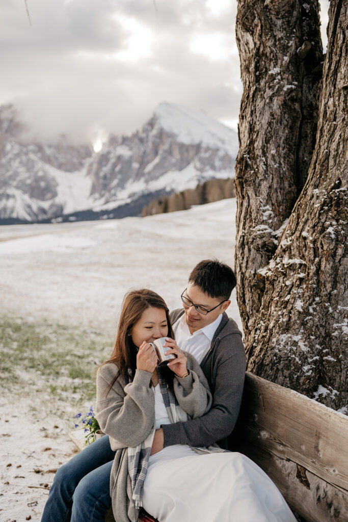 Couple drinking coffee with snowy mountain backdrop.