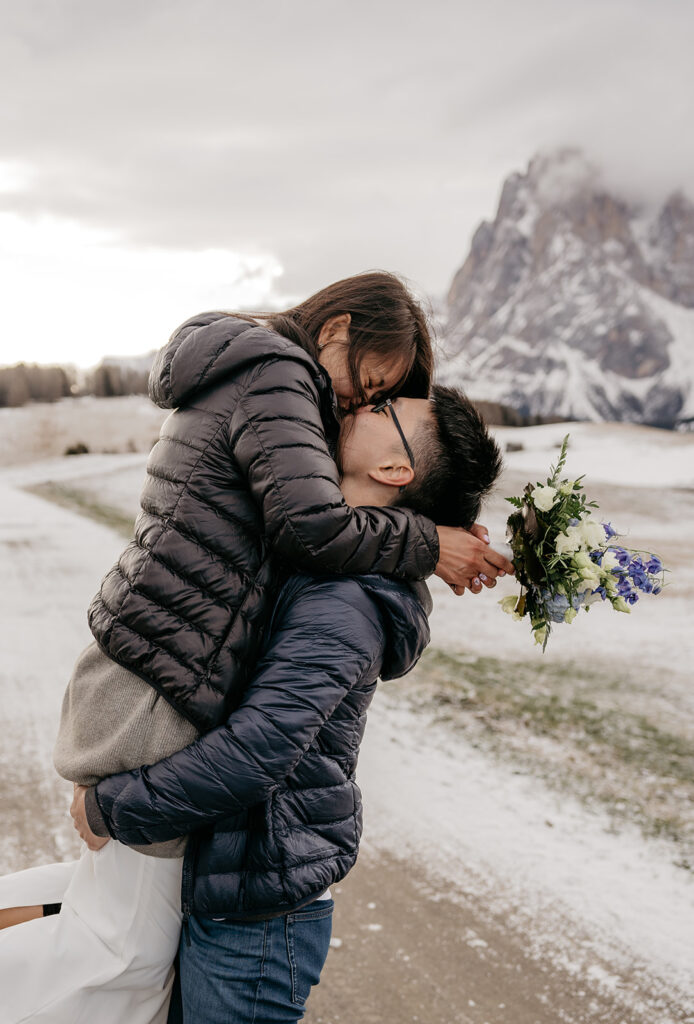 Couple embracing with mountain background, holding flowers