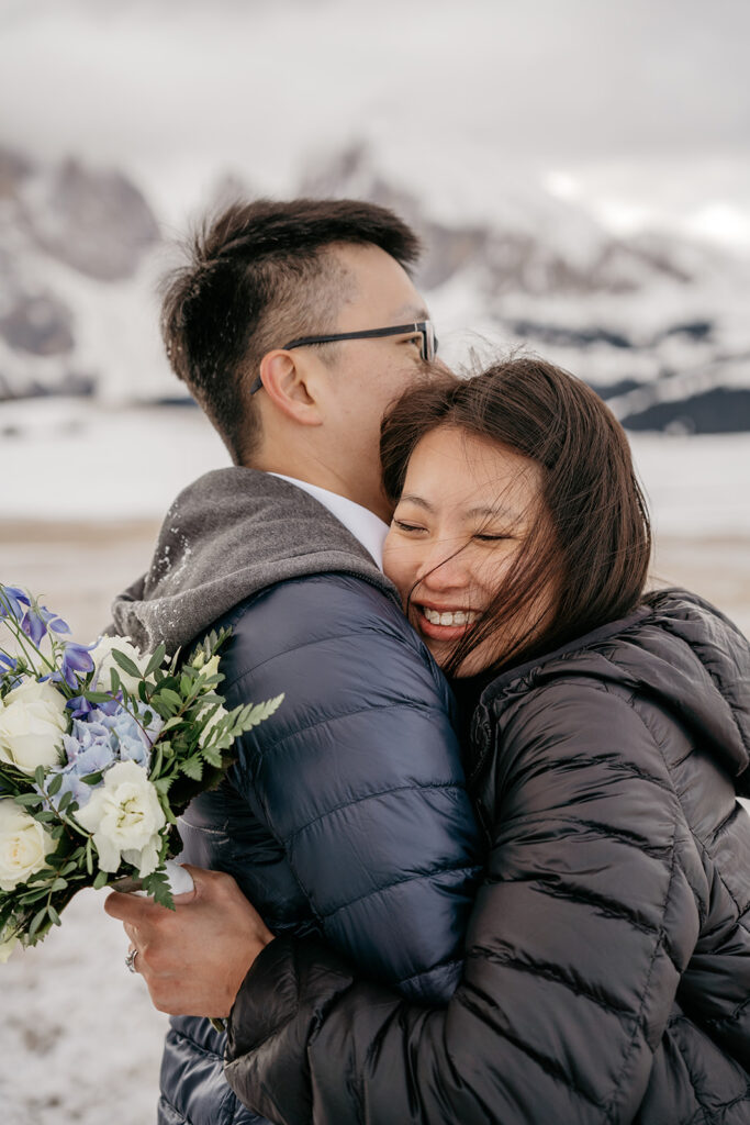 Couple hugging joyfully with bouquet in snow