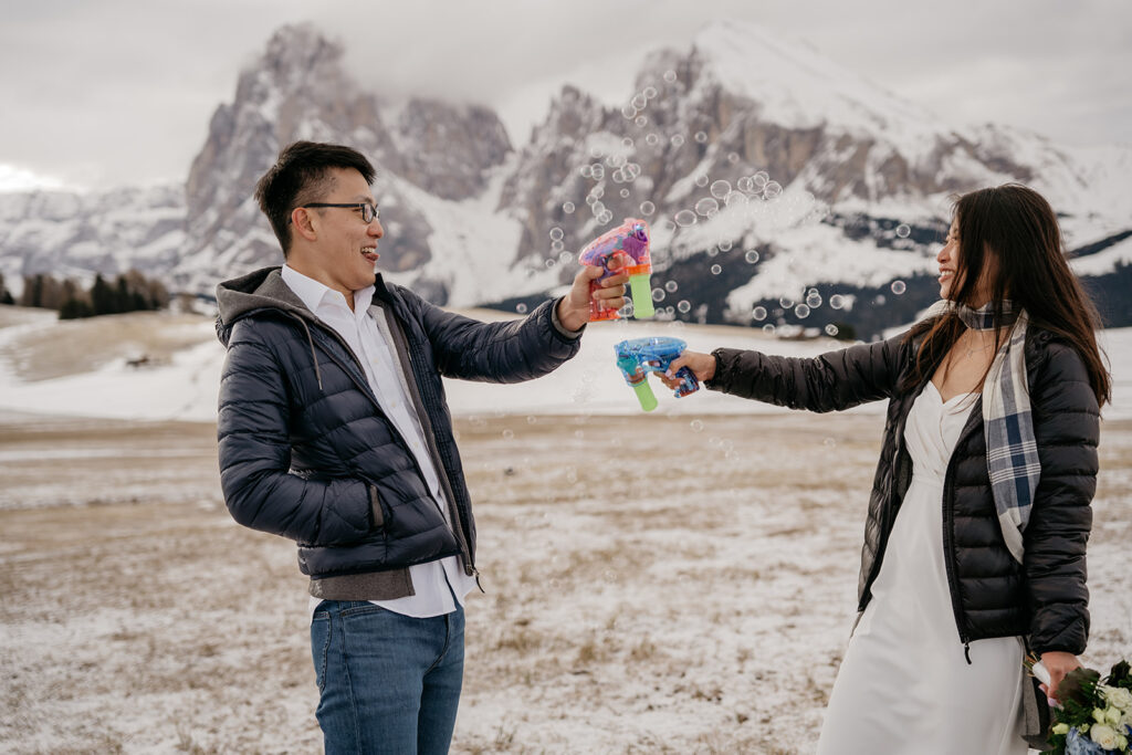 Couple playing with bubble guns in snowy mountains.