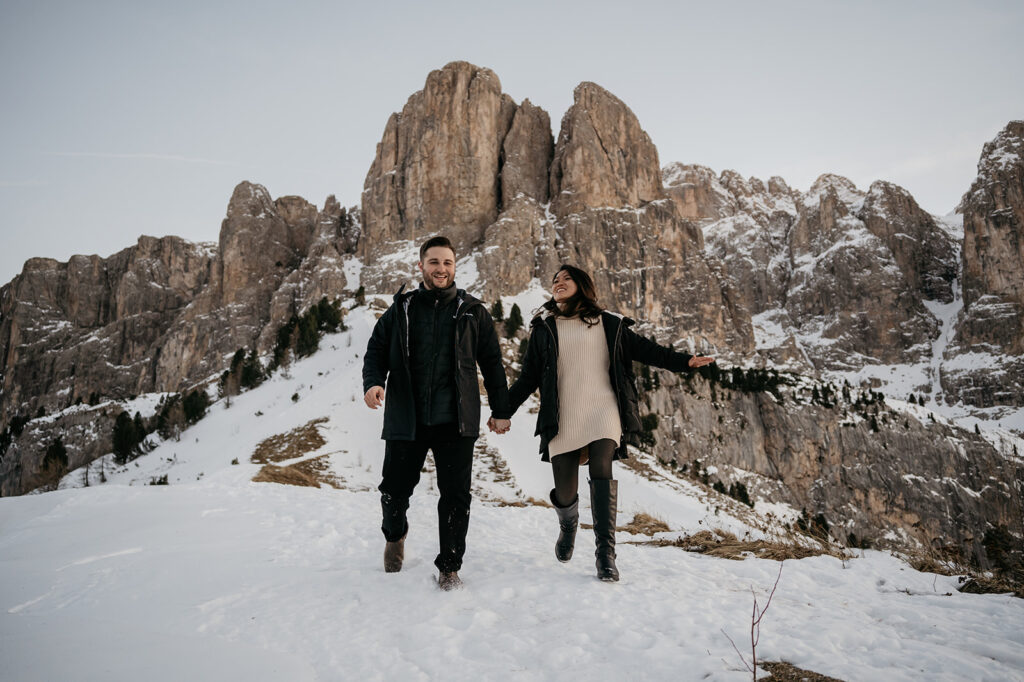 Couple walking in snowy mountains, holding hands joyfully.