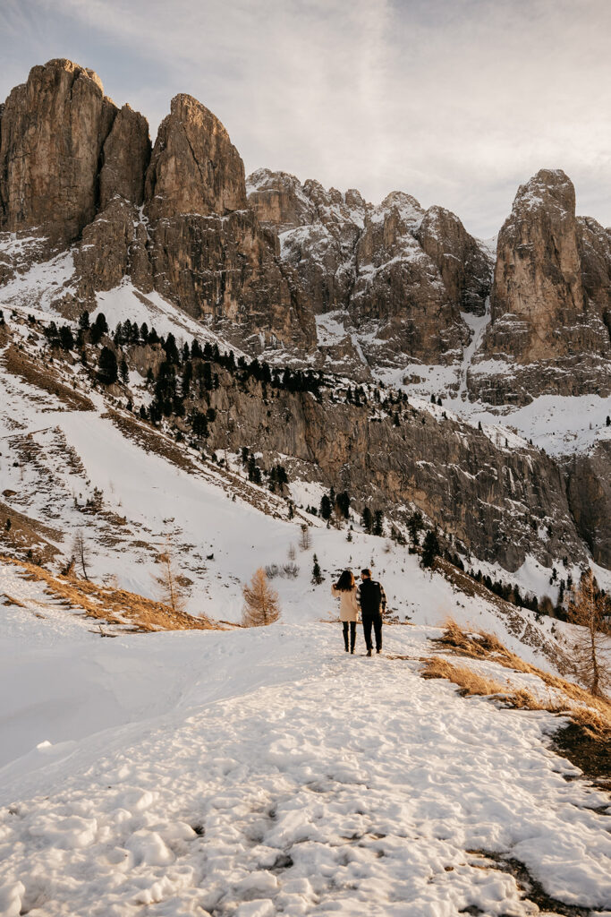 Couple walking on snowy mountain trail at sunset