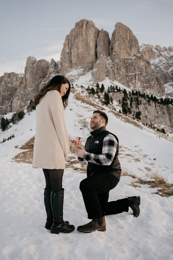 Marriage proposal on snowy mountain backdrop.