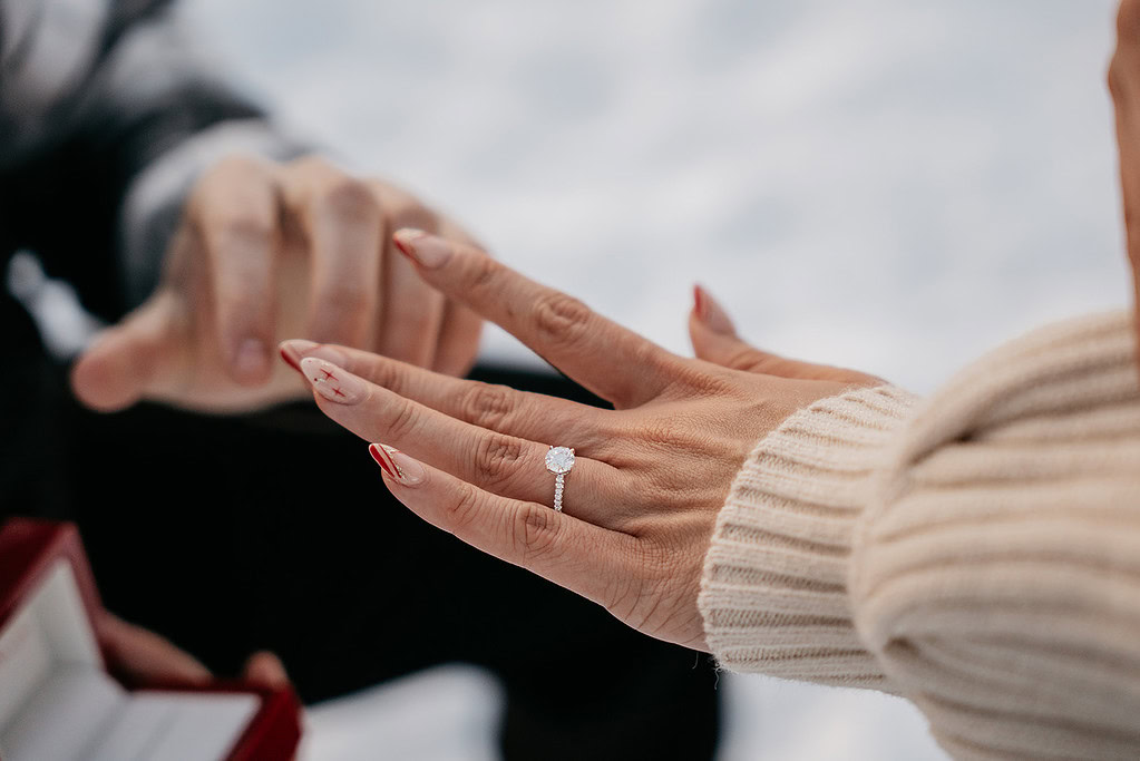 Person wearing diamond engagement ring outdoors.