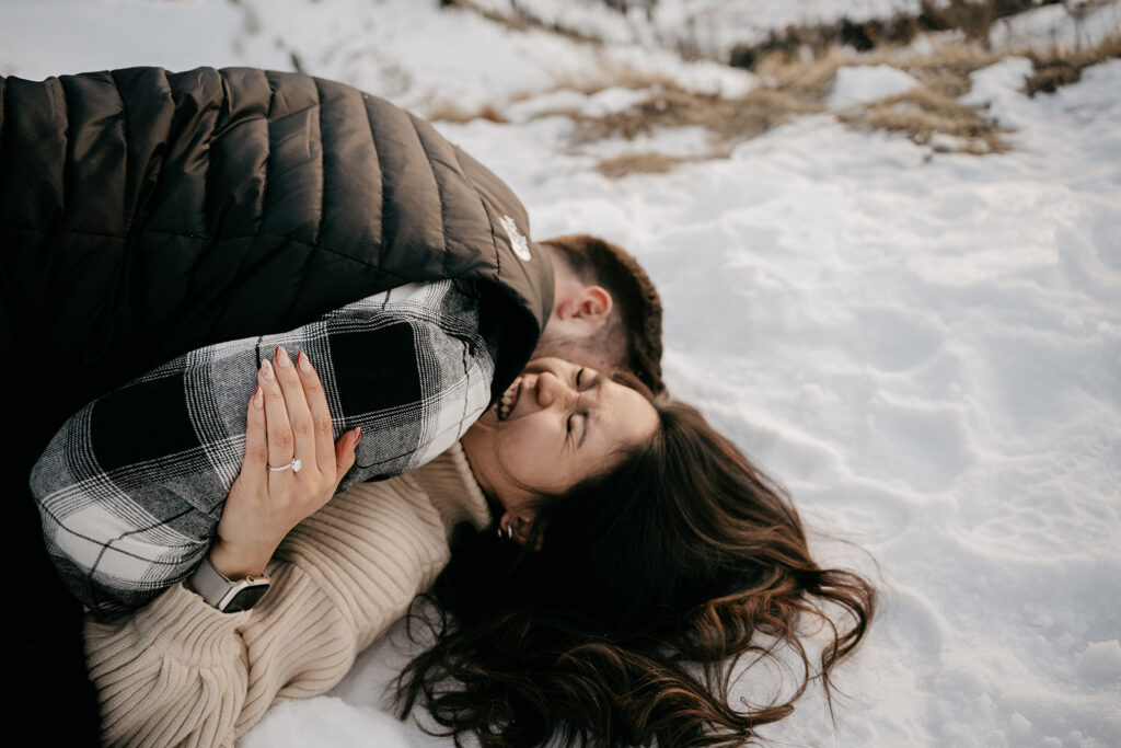 Couple laughing and hugging on snowy ground.